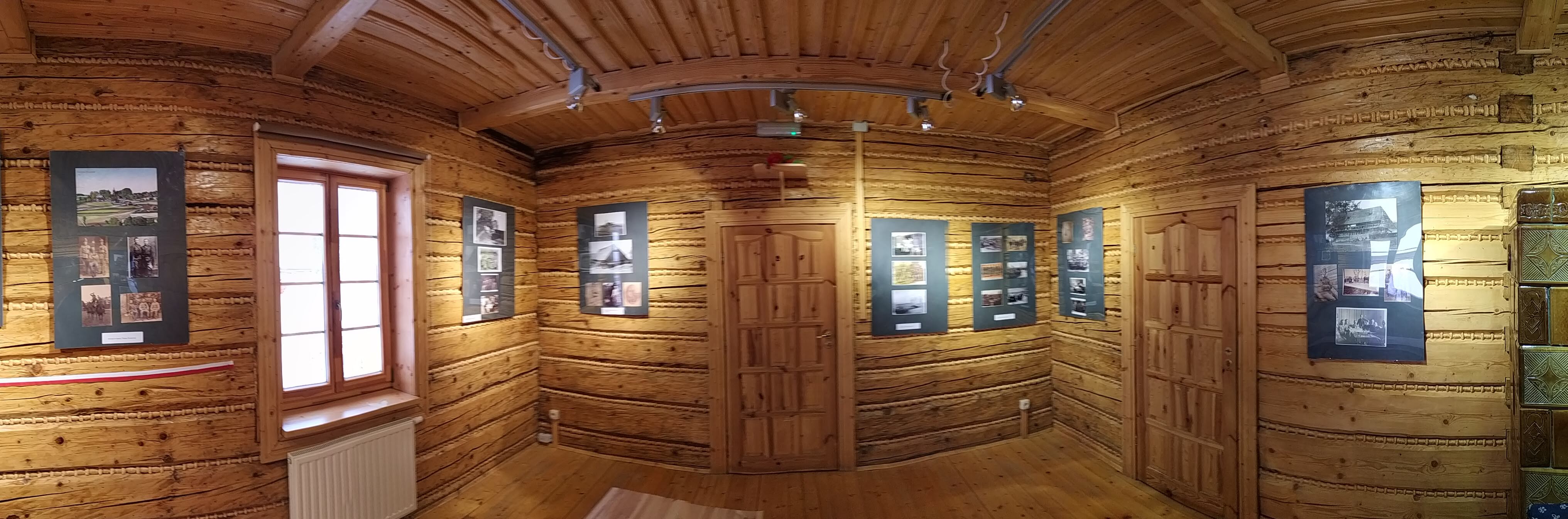 zdjęcie panoramiczne przedstawiające pomieszczenie wystawowe z wiszącymi antyramami, w których umieszczono kopie fotografii oraz opisy